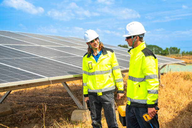 istock Two engineers wearing safety helmets and reflective jackets inspect a solar panel installation. One uses a drill tool, while the other checks the panel surface under a bright, sunny sky. 2192688140