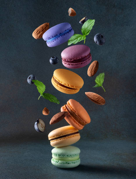 Levitating colored macaroons with mint leaves, almonds and blueberries on a dark blue background