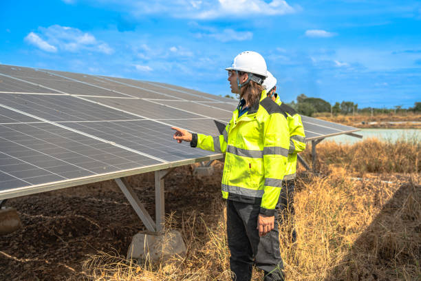istock Two technicians in safety gear and reflective jackets inspect a solar panel installation at a solar farm. They are engaged in maintenance and operational checks under a clear blue sky. 2192688852