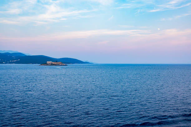 A view of a solitary island in the Adriatic Sea during sunset, with the sky painted in shades of blue and pink. The calm waters and natural scenery create a relaxing and evocative atmosphere
