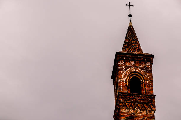 A tall brick tower with a cross on top. The sky is cloudy and the tower is the only thing visible