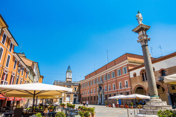 Piazza del Popolo with its column, clock tower, and surrounding buildings, is a popular gathering spot in the heart of Ravenna, Italy, featuring outdoor cafes and restaurants