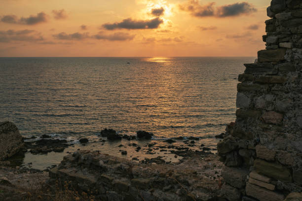 A serene rocky shoreline below Methoni Fortress bathed in warm sunlight reflecting on the Ionian Sea during a picturesque sunset.