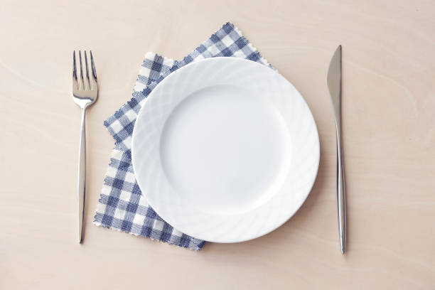 istock Empty white plate with blue fabric napkin, a fork and a knife on wooden table. Top view. 2192702071