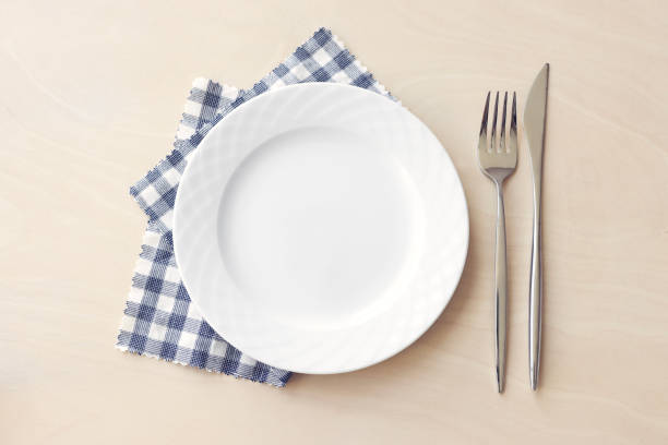 istock Empty white plate with blue fabric napkin, a fork and a knife on wooden table. Top view. 2192702076