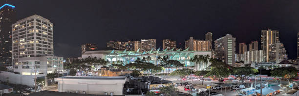 Hawaii  United States June30, 2024:  This photograph captures a scenic view of a hotel in Honolulu at dusk. The image showcases the hotel's illuminated facade, towering over the city skyline and framed by silhouetted palm trees. The warm lights of the hotel contrast with the fading blue of the evening sky, creating a captivating urban and tropical atmosphere.