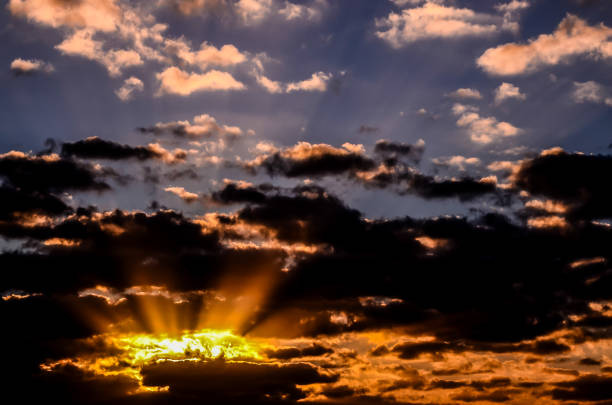The sky is filled with clouds and the sun is shining through them. The sun is creating a beautiful, warm glow in the sky