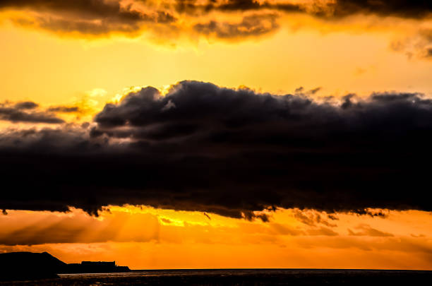 The sky is orange and the clouds are dark. The sun is setting and the sky is filled with clouds