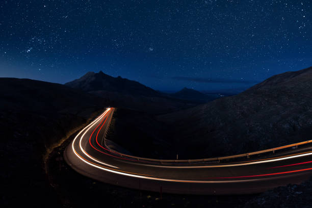 Car trails lights on a mountain road under a starry sky