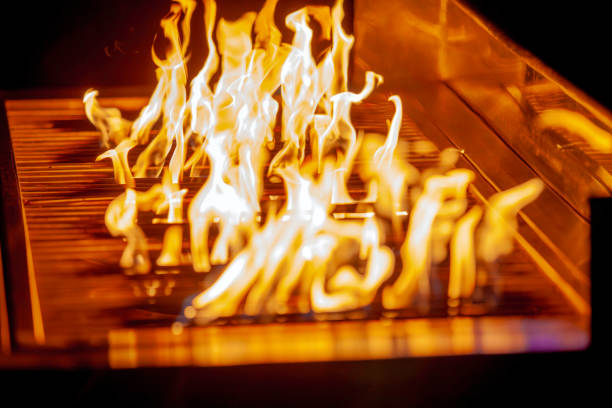 Vivid Flames on BBQ Grill with Intense Yellow Fire Up A close-up of intense yellow flames dancing on a BBQ grill, creating a captivating visual effect. The reflective metal surface enhances the fiery glow, evoking a sense of heat and energy. The image captures the essence of outdoor grilling and barbecue preparation, making it perfect for themes of culinary arts, summer gatherings, and food events. The fiery movement and vibrant colors add a dramatic and artistic flair. dangerous steak stock pictures, royalty-free photos & images