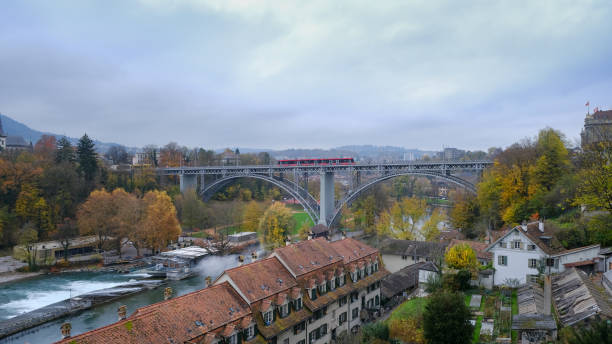 Viewpoint of Bern with Aare river and distant bridge with red tram passing on a cloudy day, Switzerland