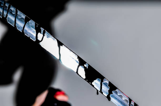 A person is holding a knife with black and white stripes on it. The knife is dripping with black paint, and the person is wearing a black shirt. The image has a dark and mysterious mood