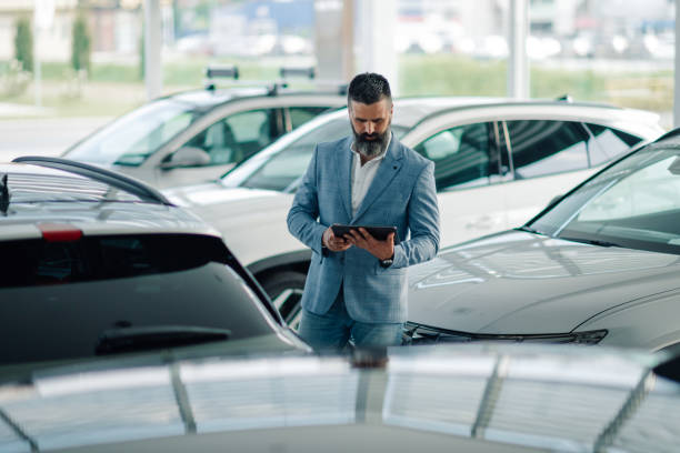 istock Car salesman using digital tablet while inspecting vehicles in dealership 2192729565