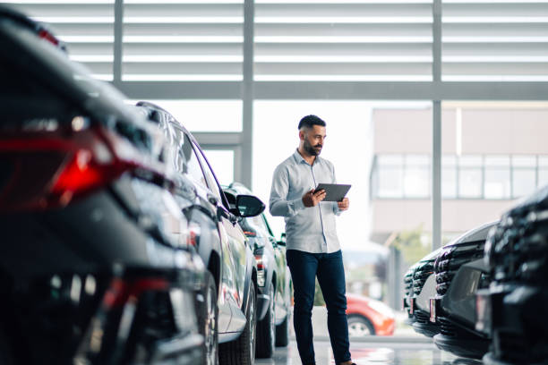 istock Car salesman using digital tablet while inspecting vehicles in showroom 2192729567