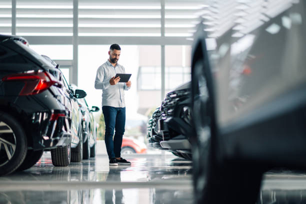 istock Car salesman using digital tablet while inspecting vehicles in dealership 2192729568