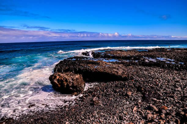 A rocky shoreline with a large rock in the middle. The water is calm and the sky is clear, creating a peaceful and serene atmosphere