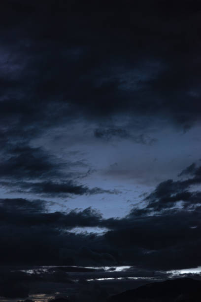 Dark, dramatic clouds dominate a twilight sky with silhouette mountains and city lights below.