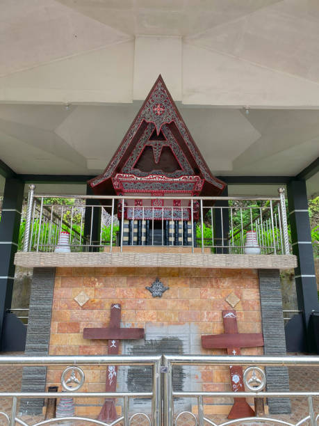 A traditional Batak structure with a distinctive roof and decorative crosses stands under a covered area.