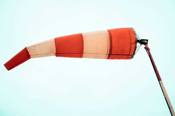 A windsock in red and white indicating wind direction, mounted on a pole with sky background. Useful in depicting aviation, weather monitoring, wind measurement, or outdoor scenes.