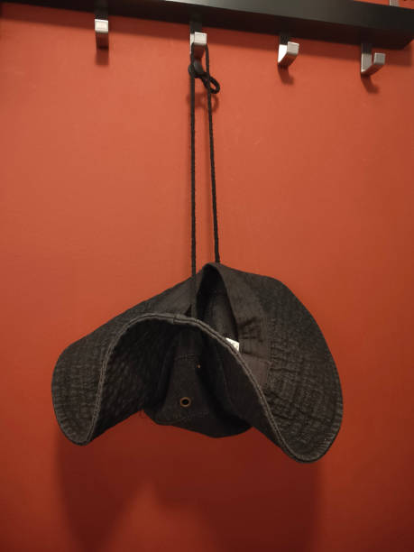 A gray denim hat hangs on the wall with black hangings A black hat is hanging from a hook on a red wall. The hat is upside down and he is upside down on purpose black hat upside down stock pictures, royalty-free photos & images