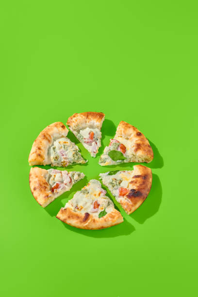 istock Sliced four cheese pizza with tomatoes and spinach on a bright green background, top view. Minimalist style, perfect for modern food photography, takeout, or casual meal. Fresh spinach leaves, vertical shot 2192755951