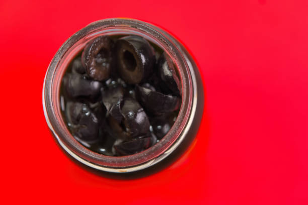 This image features a glass jar filled with black olives, with the lid open, revealing the olives inside.