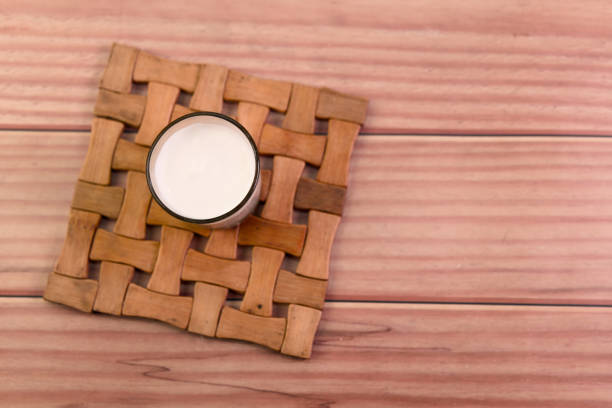 A white cup with milk in it sits on a wooden tray. The tray is made of wood and has a pattern of squares