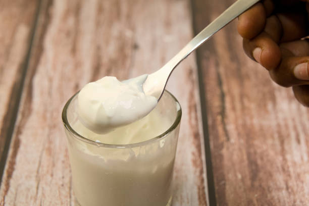 This image showcases a close-up of a hand holding a spoon filled with white, creamy yogurt.