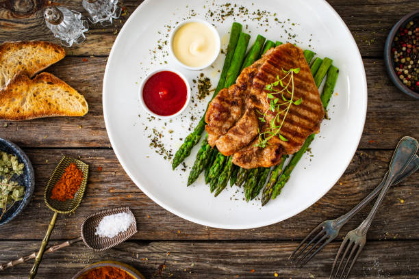 Pork loin steaks and cooked green asparagus on wooden table