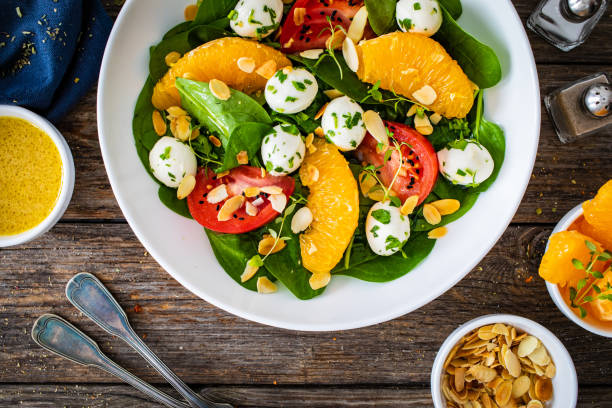 istock Mozzarella salad with leafy greens, orange and tomatoes on wooden table 2192759155
