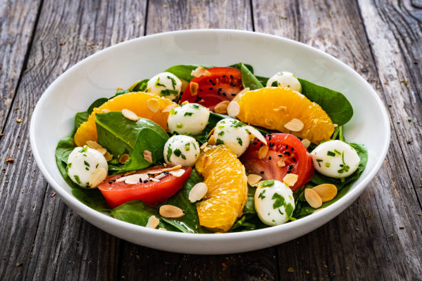 istock Mozzarella salad with leafy greens, orange and tomatoes on wooden table 2192759249