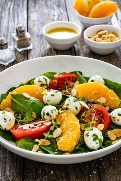 istock Mozzarella salad with leafy greens, orange and tomatoes on wooden table 2192759255