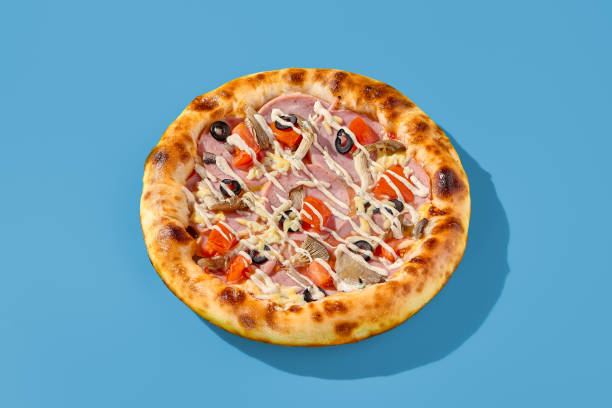 istock Thick-crust pizza with ham, mushrooms, and olives on a bright blue background. Minimalist style, side view of pizza, unhealthy food 2192761078