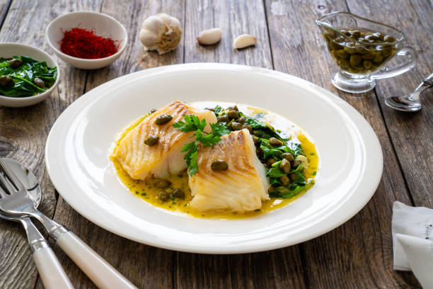 istock Fish dish - fried cod with spinach and capers in saffron sauce on wooden table 2192761084