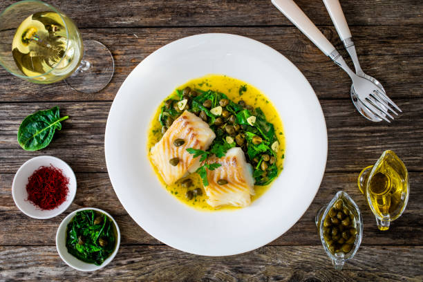 istock Fish dish - fried cod with spinach and capers in saffron sauce on wooden table 2192761116