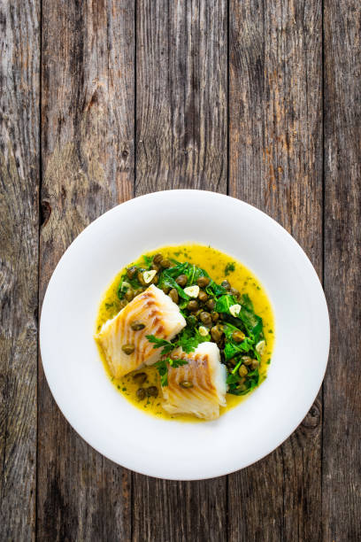istock Fish dish - fried cod with spinach and capers in saffron sauce on wooden table 2192761132