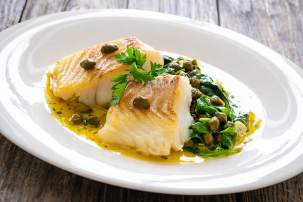 istock Fish dish - fried cod with spinach and capers in saffron sauce on wooden table 2192761168