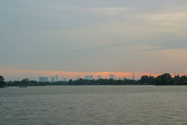 A serene lake with a distant city skyline at sunset, surrounded by trees.