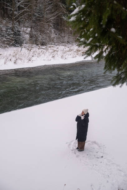 istock Person on Snowy Riverbank with Forest and Bridge 2192762559