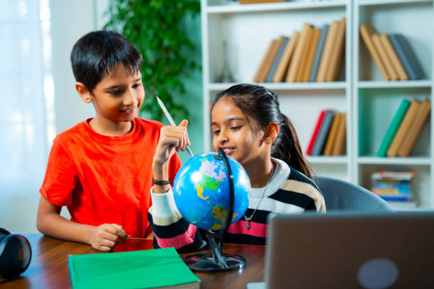 Indian siblings playing with an educational globe at home, discovering countries in a playful way