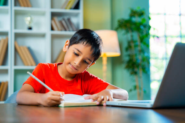 istock Indian Kid Sitting at Desk Writing Homework in Notebook at Home  Learning and Education Concept 2192763790