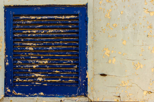 The old blue metal grate is surrounded by textured yellow paint, exhibiting a rustic and worn appearance and evoking a sense of decay and vintage character. It is suitable for concepts depicting age, texture, and history.