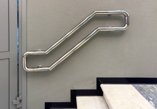 A metal railing with a silver color. The railing is attached to a wall. The railing is curved and has a shiny appearance