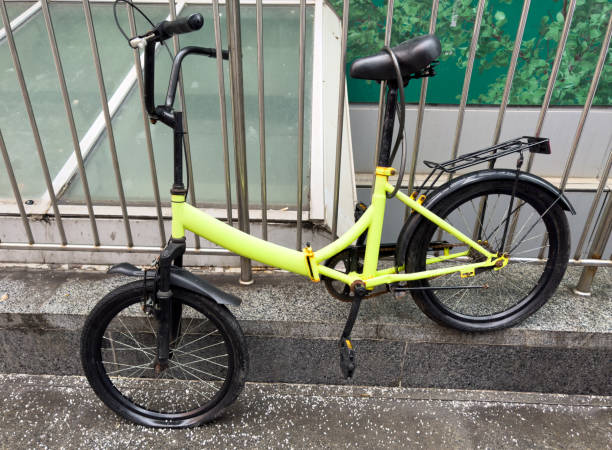 A yellow bicycle with a black seat and a black handlebar. The bike is parked on a sidewalk next to a metal fence