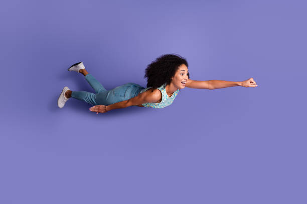 Dynamic young woman posing as a superhero on a purple backdrop, embodying confidence and joy