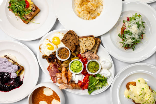 istock A vibrant breakfast spread featuring various dishes: poached eggs, toast, meats, fresh vegetables, and colorful garnishes, all presented on white plates, ideal for food-related themes. 2192779018