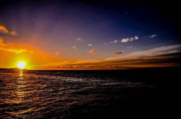 The sun is setting over the ocean, casting a warm glow on the water. The sky is filled with clouds, creating a serene and peaceful atmosphere