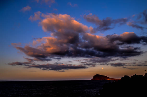 A beautiful sunset with a large moon in the sky. The clouds are dark and the sky is blue