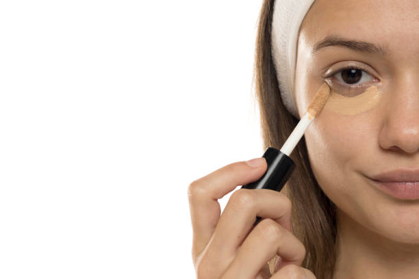 istock Beauty. Young woman applying cconcealer under her eyes on a white background. Half face. 2192787090