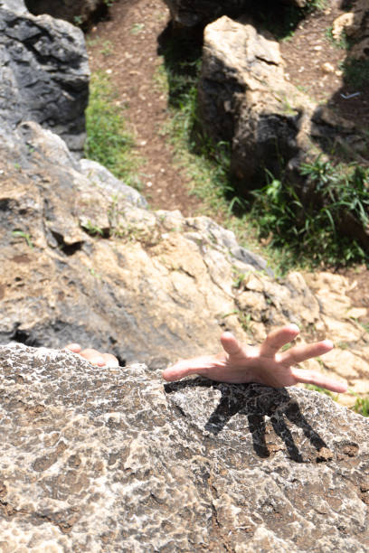A hand reaches up to grip a rough rock edge, with a blurred path in the background.